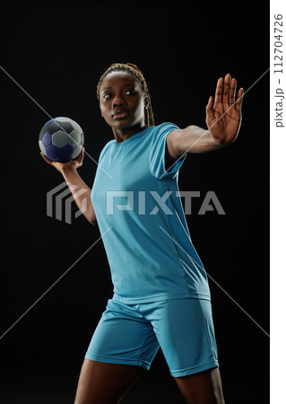 Dramatic action shot of African American female football player passing ball against black background with intense face expression 112704726