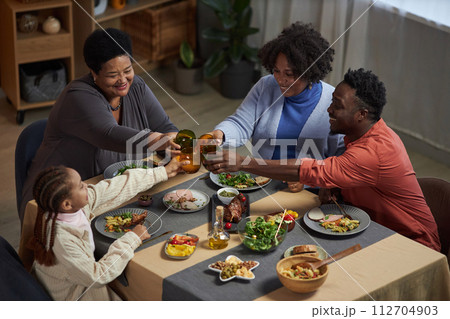 High angle portrait of three generation African American family enjoying dinner together sitting at table at home and clinking glasses in celebration 112704903