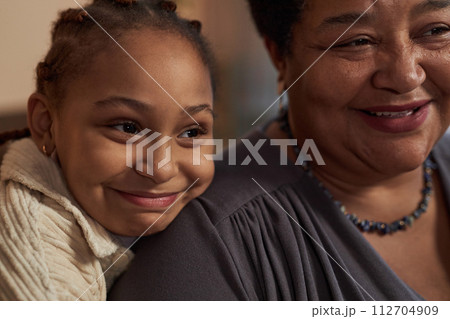 Close up portrait of cute African American little girl embracing grandmother and resting head on her shoulder 112704909