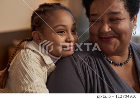 Close up portrait of cute African American little girl embracing smiling grandmother at home Close up portrait of cute African American little girl embracing smiling grandmother at home 112704910