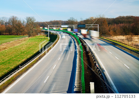 Long exposure shot of busy highway with silhouettes of driving cars on road. Traffic on motorway with motion blurred cars 112705133