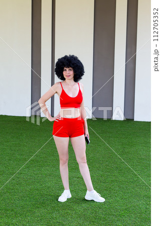 An athletic woman posing on a green lawn near a building An athletic woman posing on a green lawn near a building 112705352