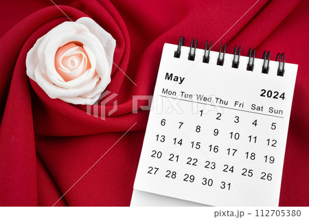May 2024 desk calendar and pink rose on red textile. 112705380