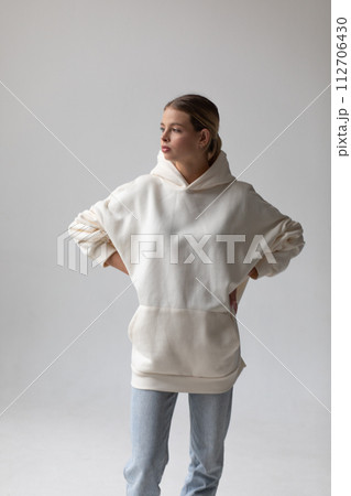 Beautiful blonde woman in a white hoodie and blue jeans posing on a white background 112706430