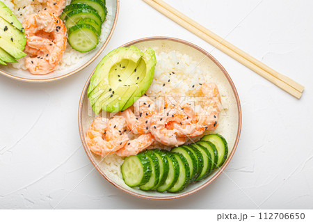 Two white ceramic bowls with rice, shrimps, avocado, vegetables and sesame seeds and wooden sticks on white concrete stone background top view. Healthy asian style poke bowl Two white ceramic bowls with rice, shrimps, avocado, vegetables and sesame seeds and wooden sticks on white concrete stone background top view. Healthy asian style poke bowl 112706650