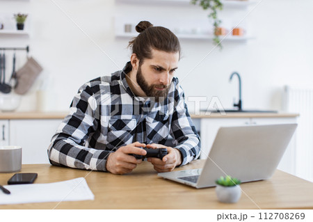 Caucasian guy in checkered shirt using remote console for playing video games. 112708269
