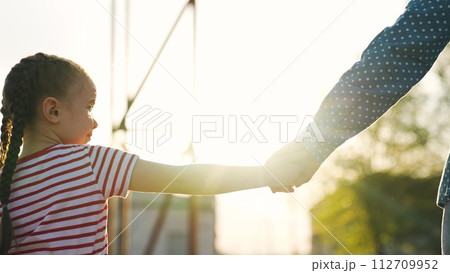 Confident adorable baby girl walking outdoor summer park sky with mother holding hands closeup back view. Cute female kid child enjoy happy childhood relaxing outdoor at bright sun sunrise sunset 112709952