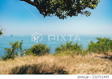 A beautiful blue ocean with sailboats in the distance. The sky is clear and the sun is shining A beautiful blue ocean with sailboats in the distance. The sky is clear and the sun is shining 112711445