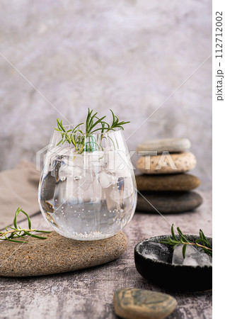 Gin tonic with ice and rosemary in a glass on a stone on the table vertical view 112712002