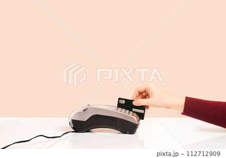 Customer hand near bar counter make payment use black credit card, hands device view, cashless method pay bills in on pink or coral background. minimalism Customer hand near bar counter make payment use black credit card, hands device view, cashless method pay bills in on pink or coral background. minimalism 112712909