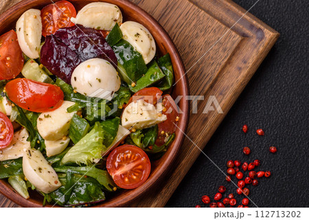 Delicious fresh caprese salad with mozzarella, tomatoes, greens with salt, spices and herbs 112713202