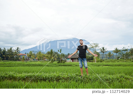 A young man poses in rice fields against the backdrop of Mount Agung volcano on the popular tourist island of Bali. 112714029