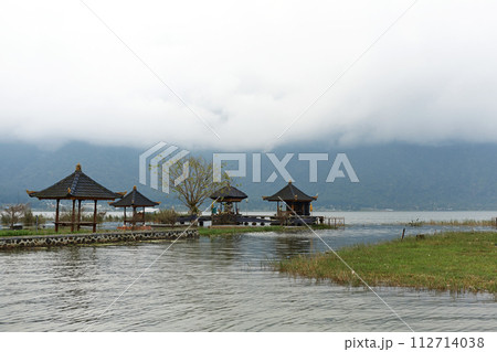 Traditional gazebos on the Bratan mountain lake in cloudy weather on the popular tourist island of Bali. Traditional gazebos on the Bratan mountain lake in cloudy weather on the popular tourist island of Bali. 112714038