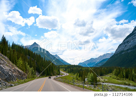 Beautiful view from a car on the Rocky Mountains in Banff National Park in Alberta. Panorama of a road in the mountains past a coniferous forest on a sunny day in summer. 112714106