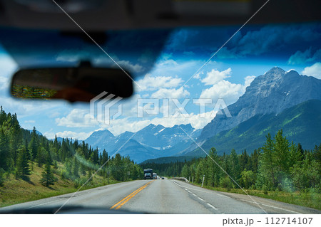 Beautiful view from a car on the Rocky Mountains in Banff National Park in Alberta. Panorama of a road in the mountains past a coniferous forest on a sunny day in summer. 112714107