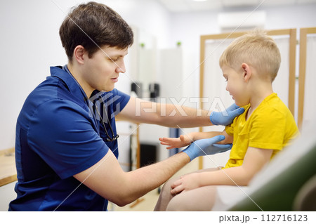 A cute toddler boy with his mother are at an appointment with a pediatrician. The doctor orthopedist is examines joints of a little patient. 112716123