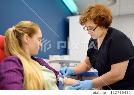 A nurse taking a blood from a young woman for examination in a modern laboratory or hospital. Young adult girl donor is at the time of donation A nurse taking a blood from a young woman for examination in a modern laboratory or hospital. Young adult girl donor is at the time of donation 112716430
