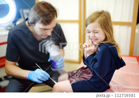 A caring doctor checks moles on the skin of a small child. Dermatologist remove of benign tumors with liquid nitrogen for cute preschooler girl. Baby fears of treat. 112716581