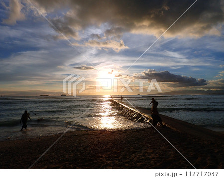 People walk along jetty path into the ocean during Sunset in Waikiki People walk along jetty path into the ocean during Sunset in Waikiki 112717037