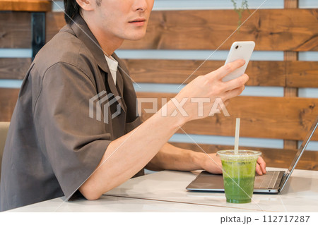 カフェでスマホとパソコンを使う若いアジア人男性 カフェでスマホとパソコンを使う若いアジア人男性 112717287