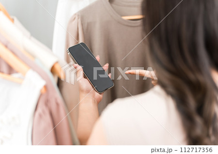 アパレルショップ・雑貨屋でスマートフォンを見ながら買い物をする女性客 112717356