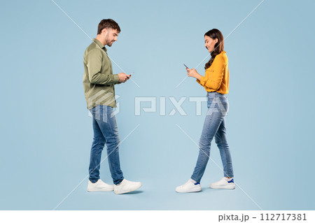 Man and woman in casual wear, using smartphones, walking to each other 112717381