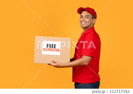 deliveryman holds cardboard box with Free Delivery label, yellow background 112717382
