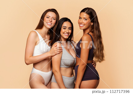 Three cheerful multiracial women in underwear embrace and smile 112717396