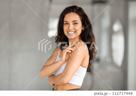 Smiling attractive brunette woman applying body lotion Smiling attractive brunette woman applying body lotion 112717449