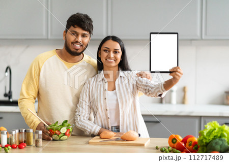 Positive young indian couple cooking at home, showing digital tablet Positive young indian couple cooking at home, showing digital tablet 112717489