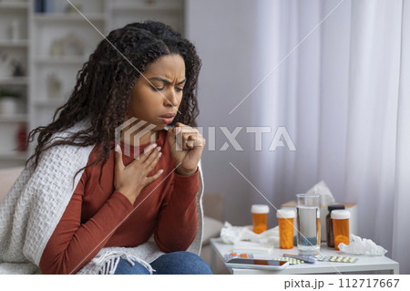 Black woman suffering cold, sitting wrapped in blanket and coughing at home Black woman suffering cold, sitting wrapped in blanket and coughing at home 112717667