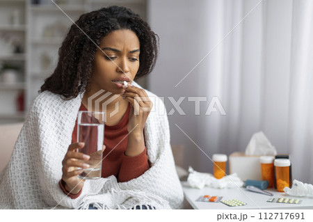 Black woman feeling unwell at home, taking pill with glass of water Black woman feeling unwell at home, taking pill with glass of water 112717691