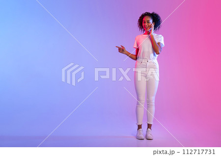 Smiling black lady pointing to side at free space on blue and pink gradient background 112717731