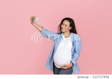 Beautiful young pregnant woman taking selfie on pink background 112717856