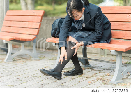 登校・下校中に脚を痛めて公園のベンチに座る中学生・高校生の女子生徒 112717876
