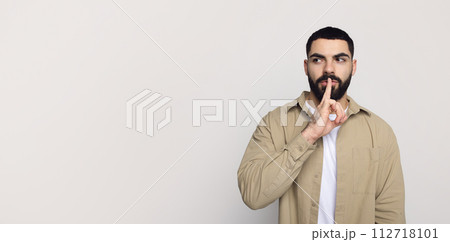 Serious handsome young middle eastern man with beard in casual make shhh gesture with finger lips 112718101