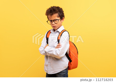 Serious black schoolboy with backpack and glasses on yellow 112718203