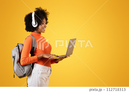 Focused young woman with afro hair and white headphones, using a laptop 112718313