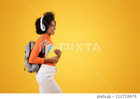 Side-view of a content young student with curly afro hair wearing white headphones Side-view of a content young student with curly afro hair wearing white headphones 112718478