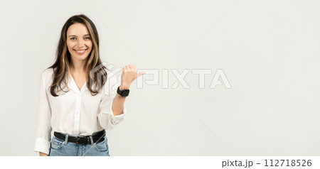 Cheerful young woman in a white blouse and blue jeans giving a thumbs up while wearing a smartwatch 112718526
