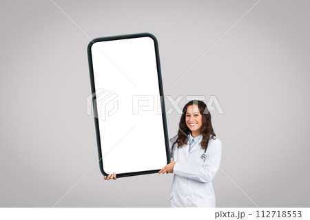 Positive european female doctor displaying huge cellphone with white empty screen, mockup 112718553