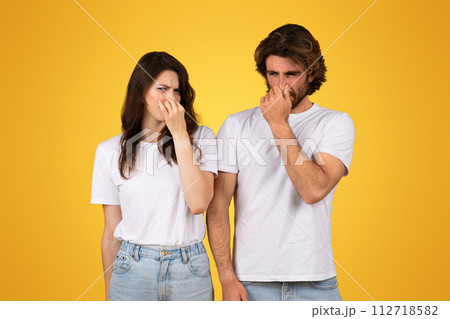 Distressed young couple in white shirts pinching their noses, displaying expressions of disgust Distressed young couple in white shirts pinching their noses, displaying expressions of disgust 112718582