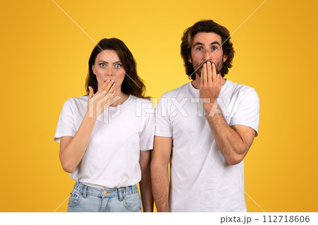 man and a woman with surprised expressions, both covering their mouths with their hands 112718606