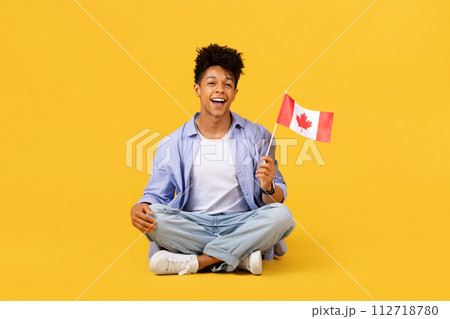 Happy black male student with Canadian flag sitting on yellow background 112718780