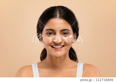 Skin Care. Young indian woman with dab of cream on her cheek Skin Care. Young indian woman with dab of cream on her cheek 112718809