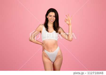 Cheerful young woman in white underwear making a perfect gesture with her hand Cheerful young woman in white underwear making a perfect gesture with her hand 112718848