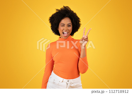Vivacious young woman with fluffy afro hair winks and flashes a peace sign Vivacious young woman with fluffy afro hair winks and flashes a peace sign 112718912