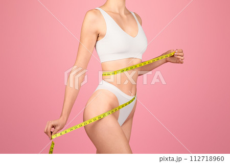 Side view of a determined woman in white lingerie measuring her perfect waist 112718960