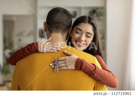 Happy young woman hugging husband and holding home keys in hand Happy young woman hugging husband and holding home keys in hand 112718961