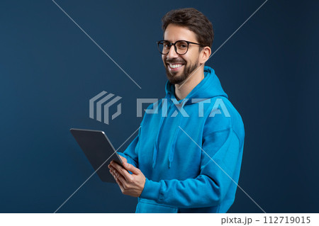 Handsome young man wearing glasses and blue hoodie using digital tablet 112719015